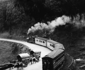 ca. 1930, Darjeeling, India --- A steam driven passenger train negotiates a bend on a narrow track which descends towards Darjeeling. Two "brake men" ride at the rear of the end carriage. --- Image by © Hulton-Deutsch Collection/CORBIS